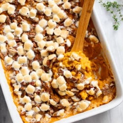A wooden spoon scooping up sweet potato casserole from a baking dish.