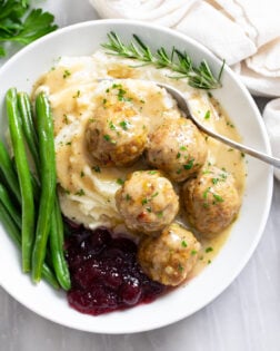 Turkey and Stuffing Meatballs on a white plate with mashed potatoes, gravy, cranberry sauce, and green beans.