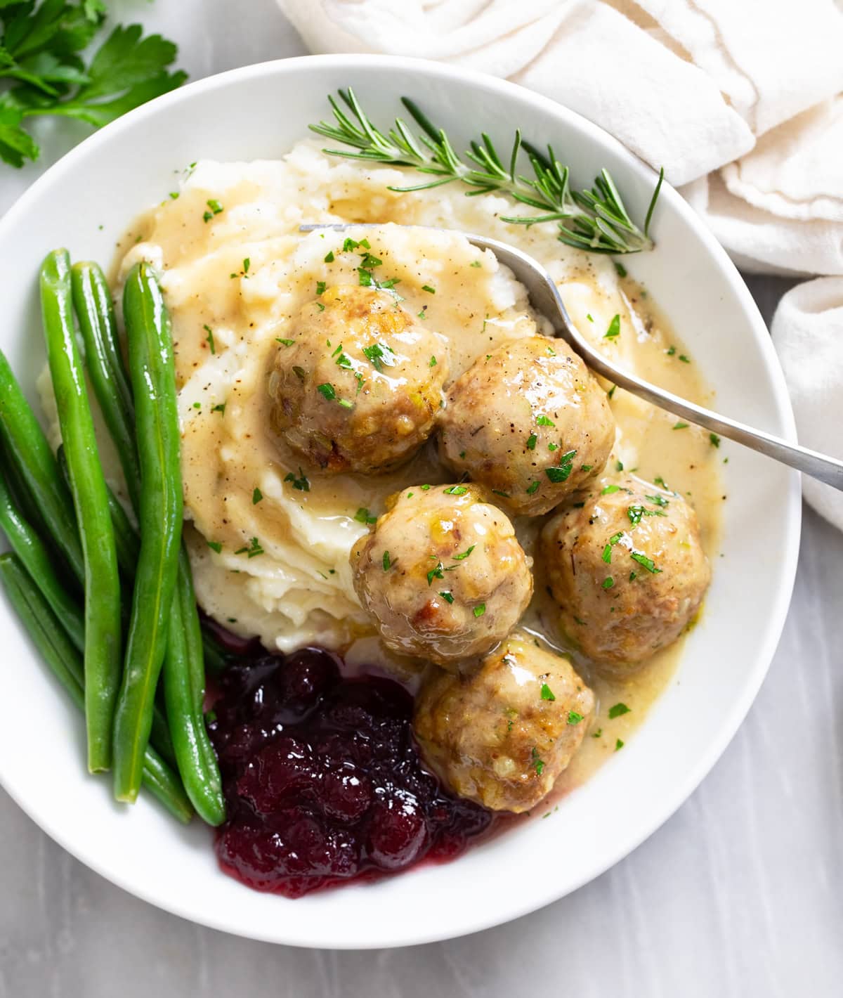 Turkey and Stuffing Meatballs on a white plate with mashed potatoes, gravy, cranberry sauce, and green beans.