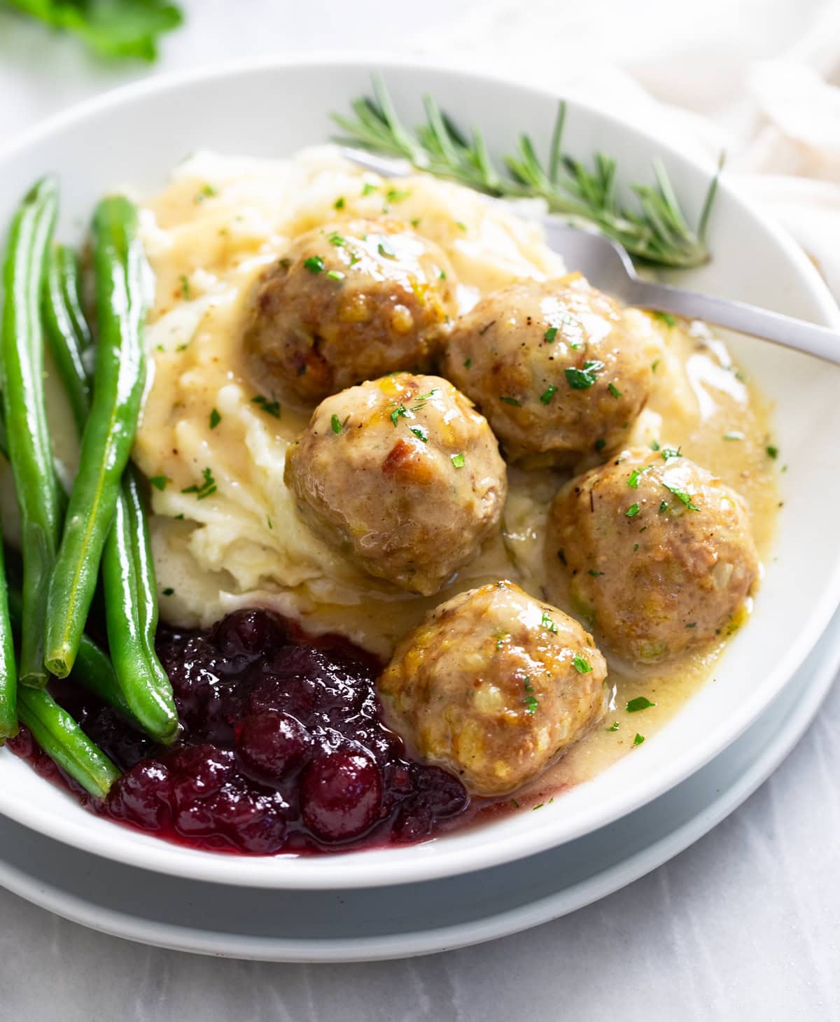 Side view of Turkey and Stuffing Meatballs on a pile of mashed potatoes with cranberry sauce and green beans.