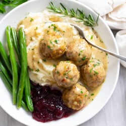 Turkey and Stuffing Meatballs on a pile of mashed potatoes with gravy, cranberry sauce, and green beans.