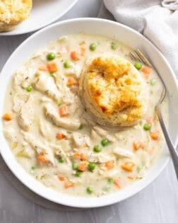 Crock Pot Chicken Pot Pie in a white bowl with a buttermilk biscuit on the side.