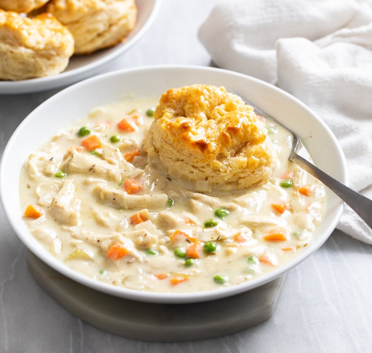 Side view of Crock Pot Chicken Pot Pie in a white bowl with a fork on the side and a biscuit on top.