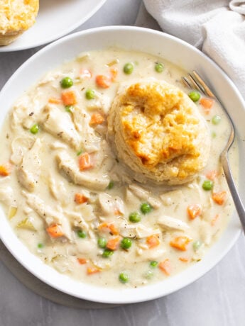 Crock Pot Chicken Pot Pie in a white bowl with a buttermilk biscuit on the side.