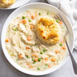 Crock Pot Chicken Pot Pie in a white bowl with a fork and a buttermilk biscuit.