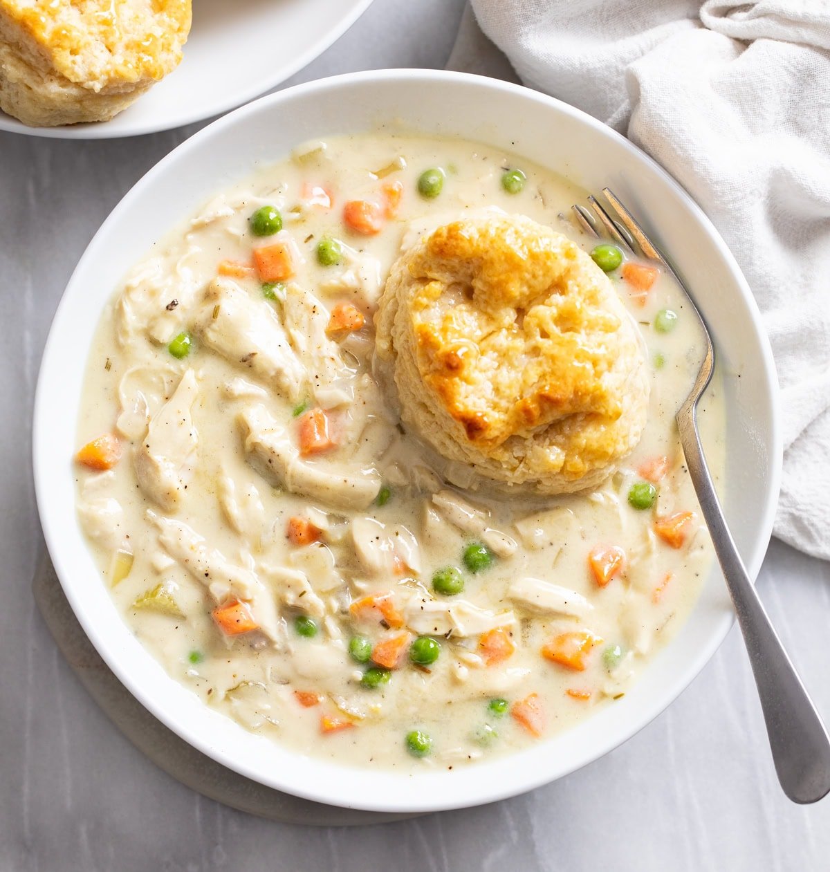 Crock Pot Chicken Pot Pie in a white bowl with a buttermilk biscuit on the side.