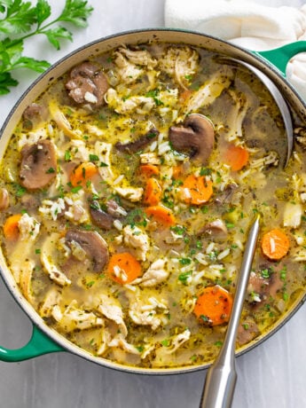 A soup pot with chicken and mushroom soup with rice in it and a ladle on the side.