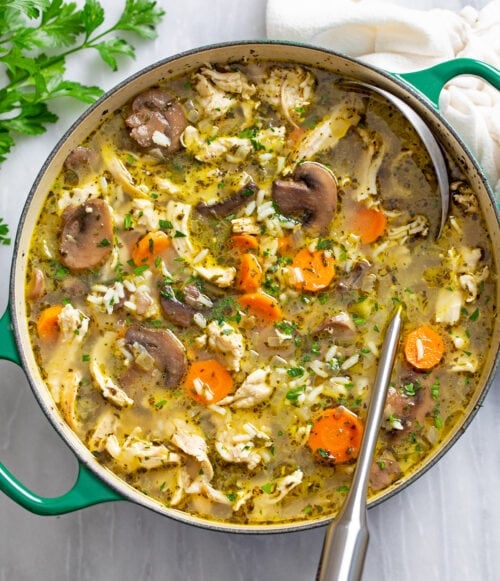 A soup pot with chicken and mushroom soup with rice in it and a ladle on the side.