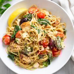 Mediterranean Pasta in a white bowl with spinach, tomatoes, chicken, feta, and olives.
