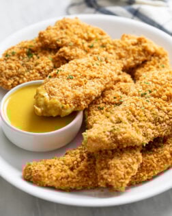 Crispy Baked Chicken Tenders on a white plate with honey mustard sauce.