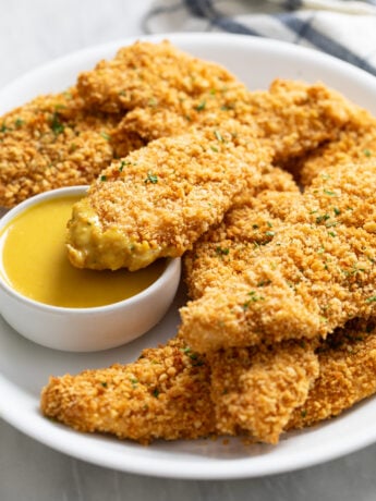 Crispy Baked Chicken Tenders on a white plate with honey mustard sauce.