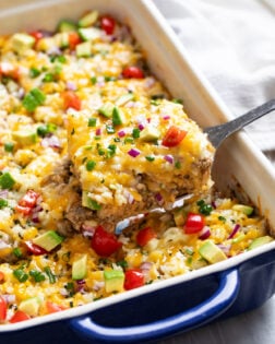 Burrito Casserole with beef, tortillas, cheese, refried beans, and rice being scooped out of a casserole dish.