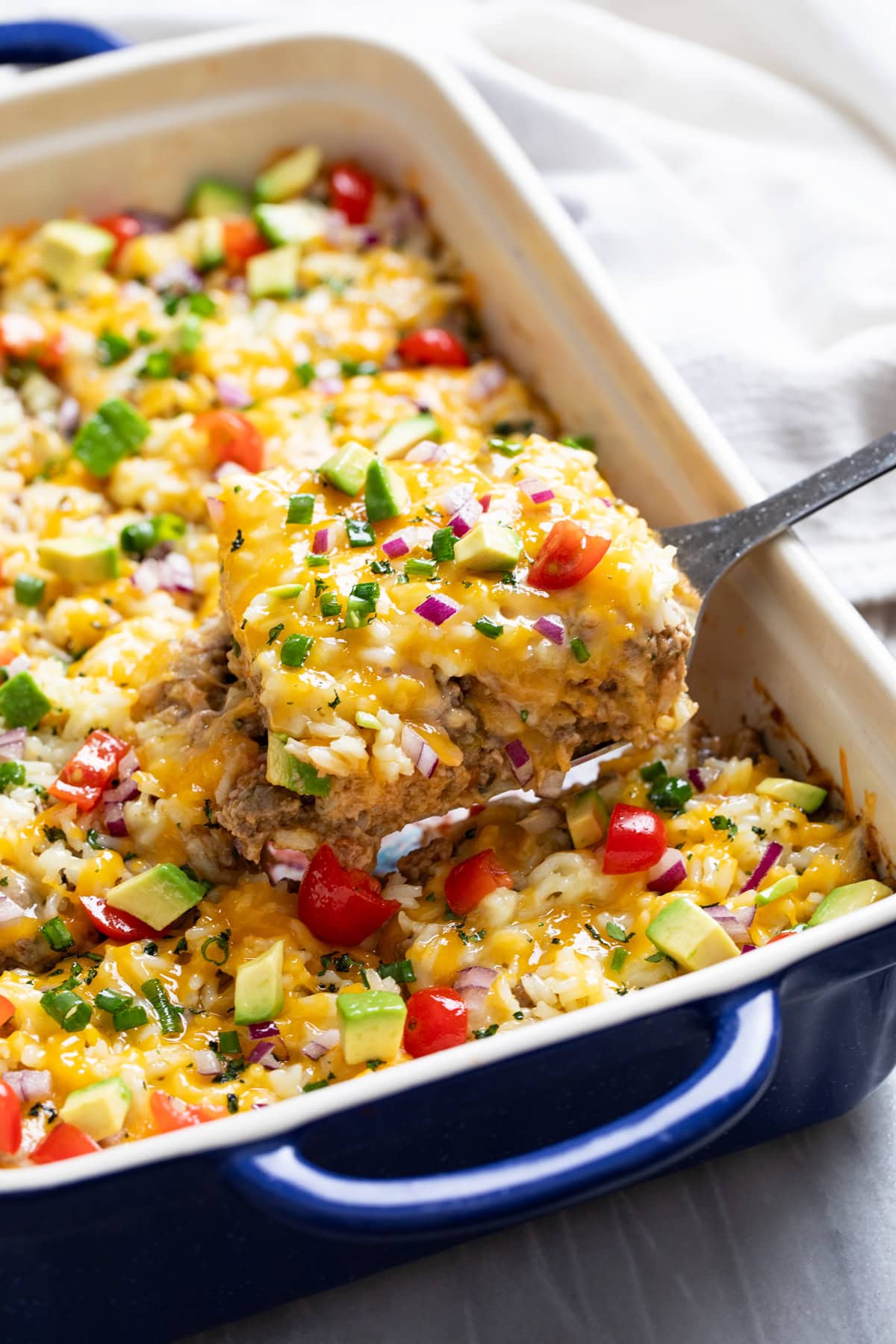 Burrito Casserole with beef, tortillas, cheese, refried beans, and rice being scooped out of a casserole dish.