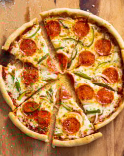 Slices of Cast Iron Skillet Pizza with pepperoni, peppers, and onions on a wooden surface.