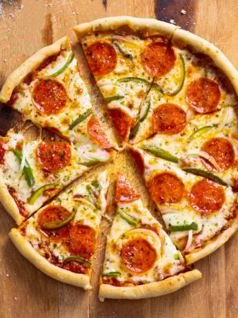 Slices of Cast Iron Skillet Pizza with pepperoni, peppers, and onions on a wooden surface.