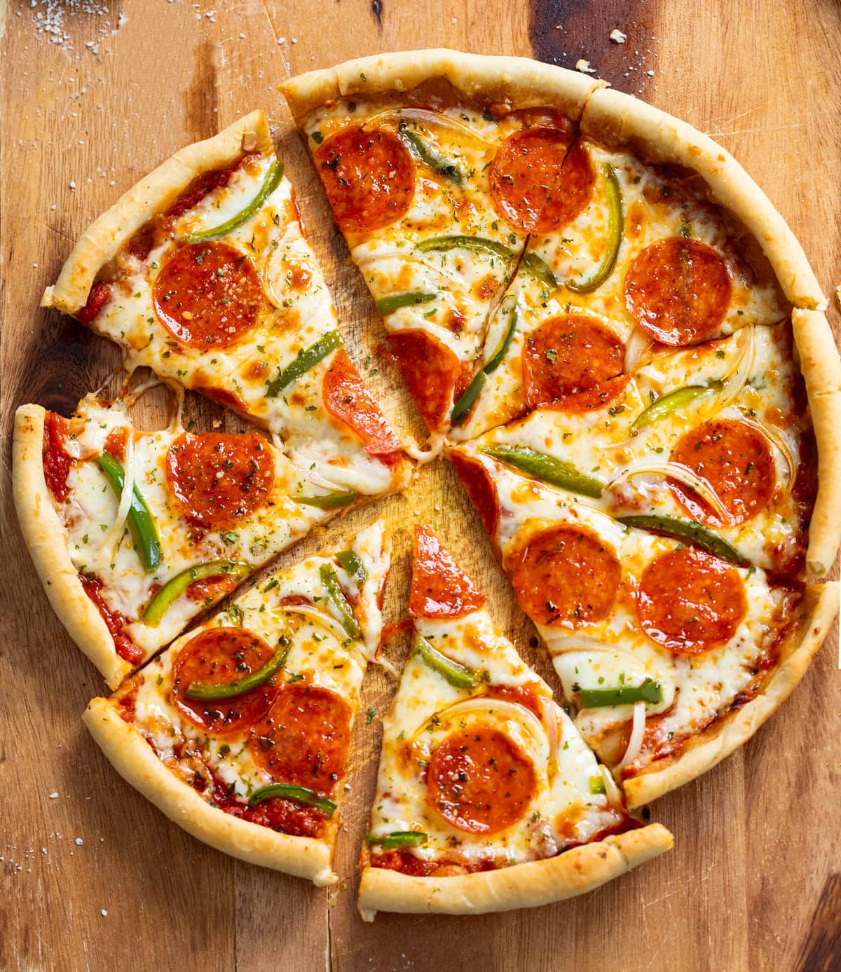 Slices of Cast Iron Skillet Pizza with pepperoni, peppers, and onions on a wooden surface.