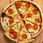 A cast iron skillet pizza on a cutting board with the slices cut up and slightly pulled apart.