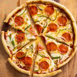 A cast iron skillet pizza on a cutting board with the slices cut up and slightly pulled apart.