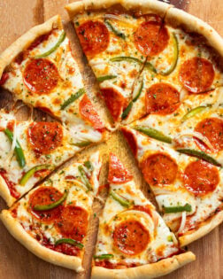 A cast iron skillet pizza on a cutting board with the slices cut up and slightly pulled apart.