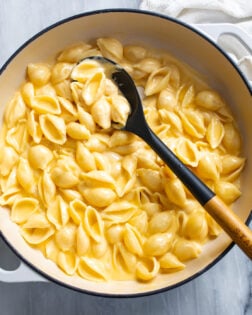 Shells and Cheese in a skillet with a a spoon scooping it up.