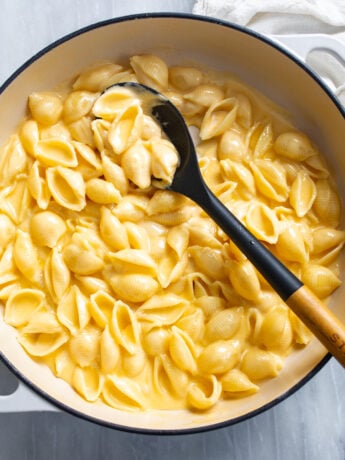Shells and Cheese in a skillet with a a spoon scooping it up.