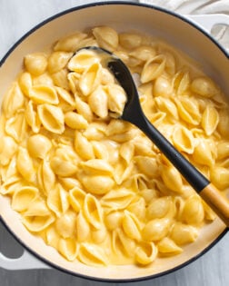 Creamy Shells and Cheese in a skillet with a spoon on the side.
