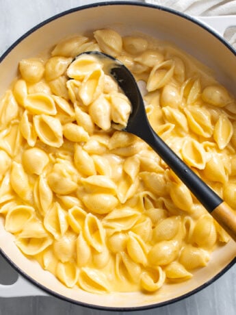 Creamy Shells and Cheese in a skillet with a spoon on the side.