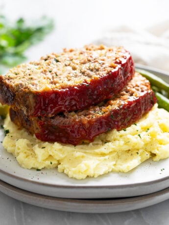 Stuffing Meatloaf on a pile of creamy mashed potatoes with green beans in the background.