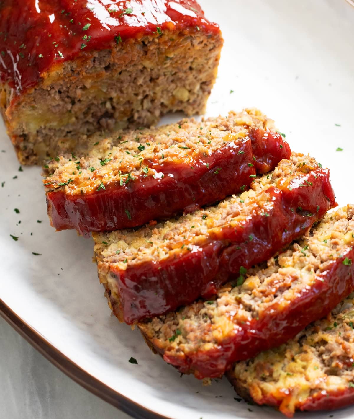 Slices of Stuffing Meatloaf on a white platter with parsley on top.