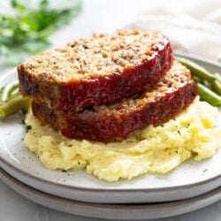 Stuffing Meatloaf on a pile of mashed potatoes with green beans behind it.