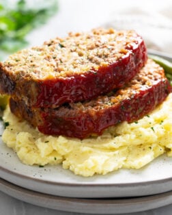 Stuffing Meatloaf on a pile of mashed potatoes with green beans behind it.
