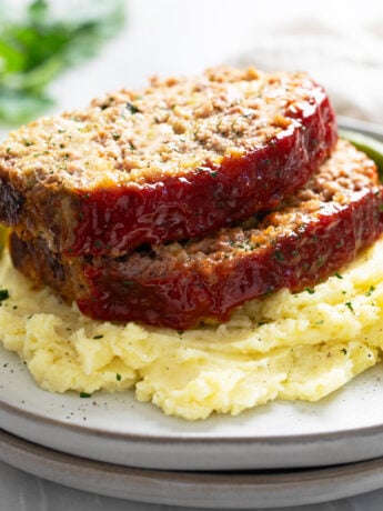 Stuffing Meatloaf on a pile of mashed potatoes with green beans behind it.