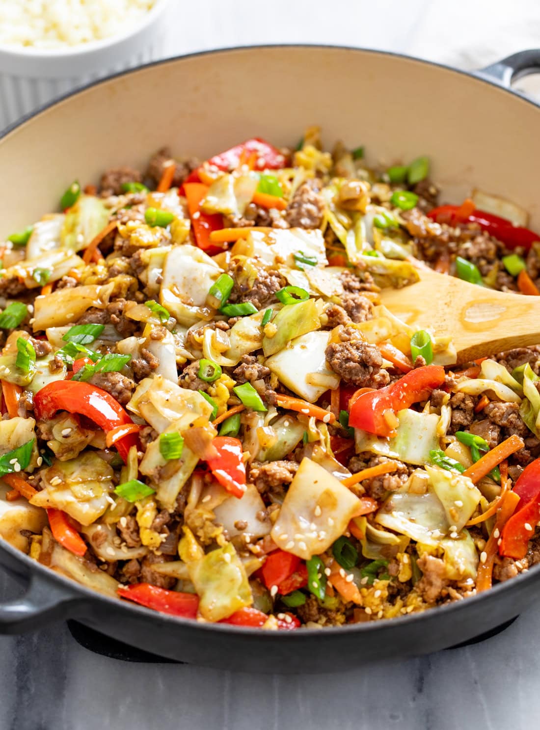 Side view of Cabbage Stir Fry in a skillet with a wooden spatula scooping it up.