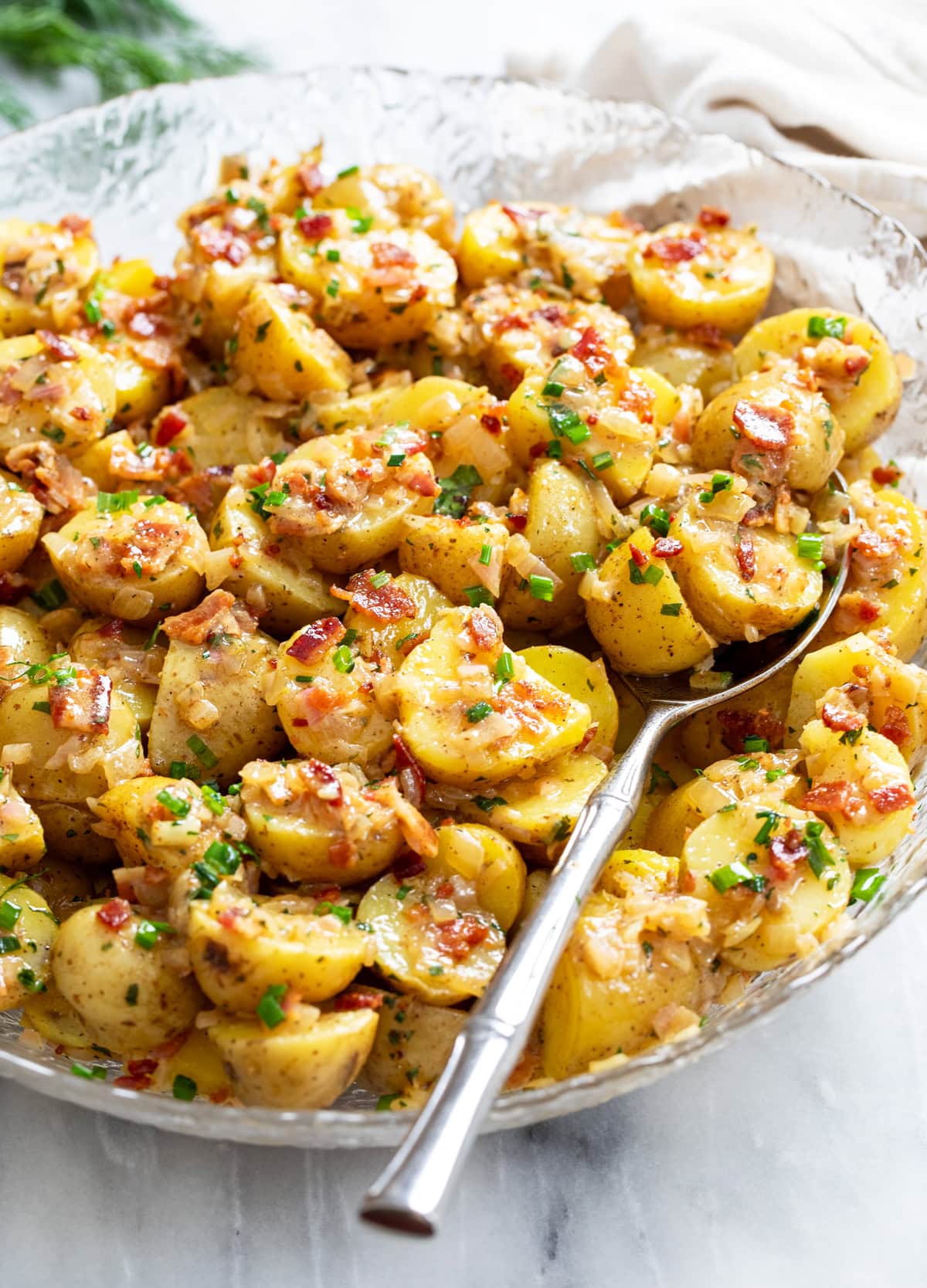 Side view of German Potato Salad in a glass bowl with a spoon on the side.