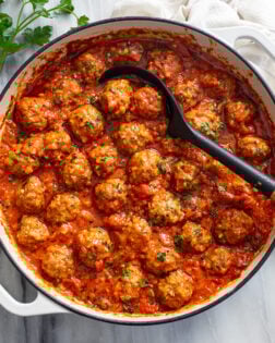 Porcupine Meatballs in a white baking dish with a spoon in the middle and parsley on the side.