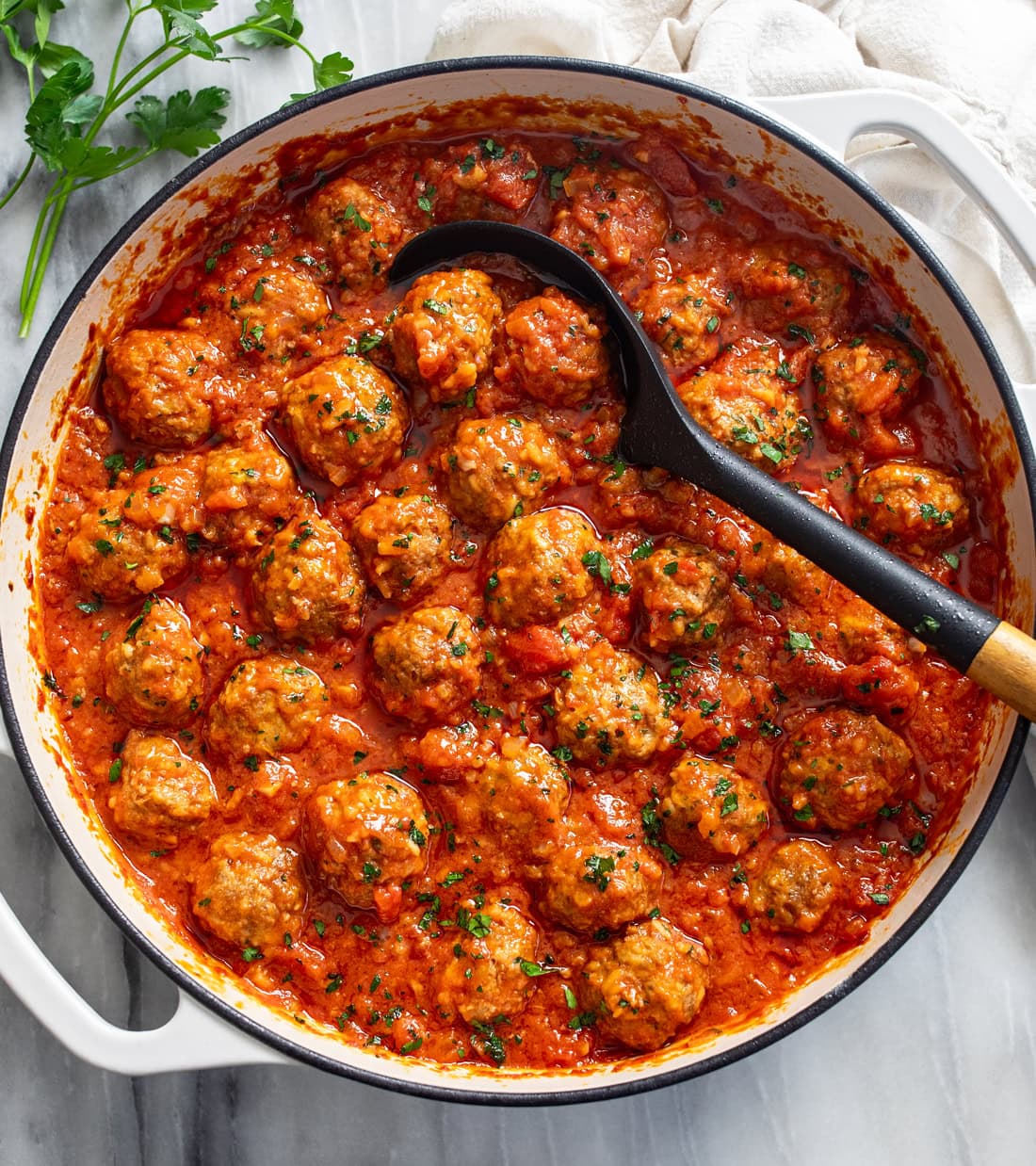 Porcupine Meatballs in a white baking dish with a spoon in the middle and parsley on the side.