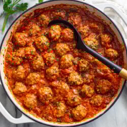 A white baking dish filled with Porcupine Meatballs in a red sauce with a spoon in the middle.
