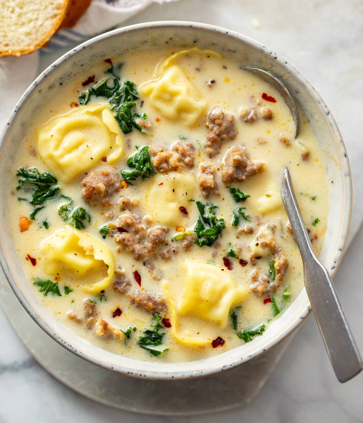 Sausage Tortellini Soup in a soup bowl with a spoon on the side.