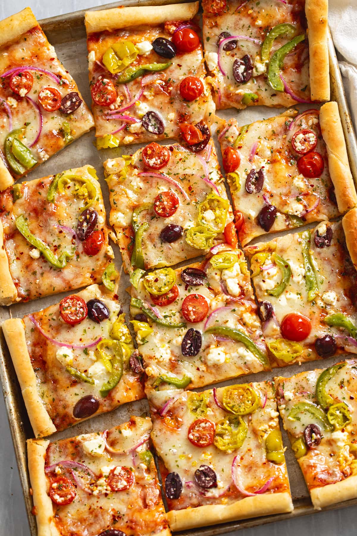 Greek Pizza cut into slices on a sheet pan topped with feta and veggies.