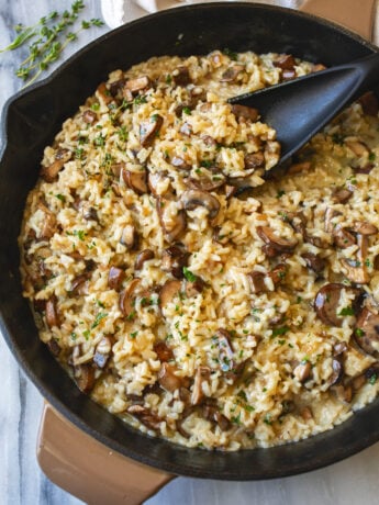 Creamy Mushroom Risotto in a skillet with fresh thyme on the side and fresh parsley on top.