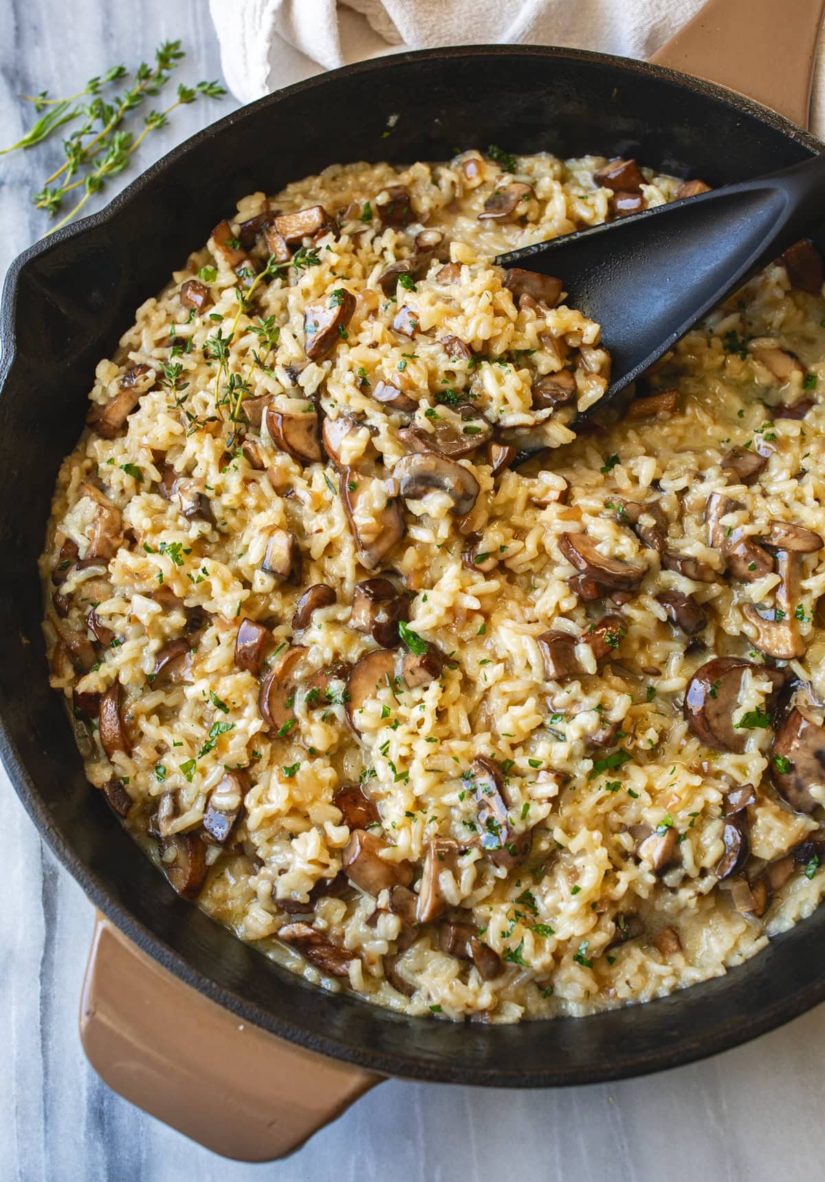 Creamy Mushroom Risotto in a skillet with fresh thyme on the side and fresh parsley on top.