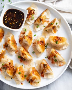 Potstickers on a white plate with chives and chili crisp on top and sauce on the side.