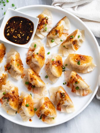 Potstickers on a white plate with chives and chili crisp on top and sauce on the side.