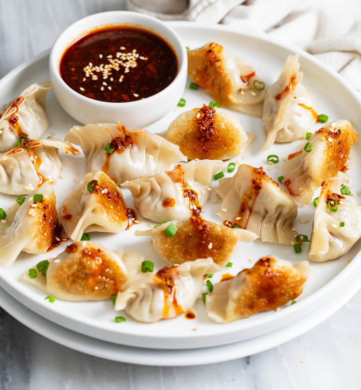Side view of Potstickers on a white plate with sauce in the back and chives on top.