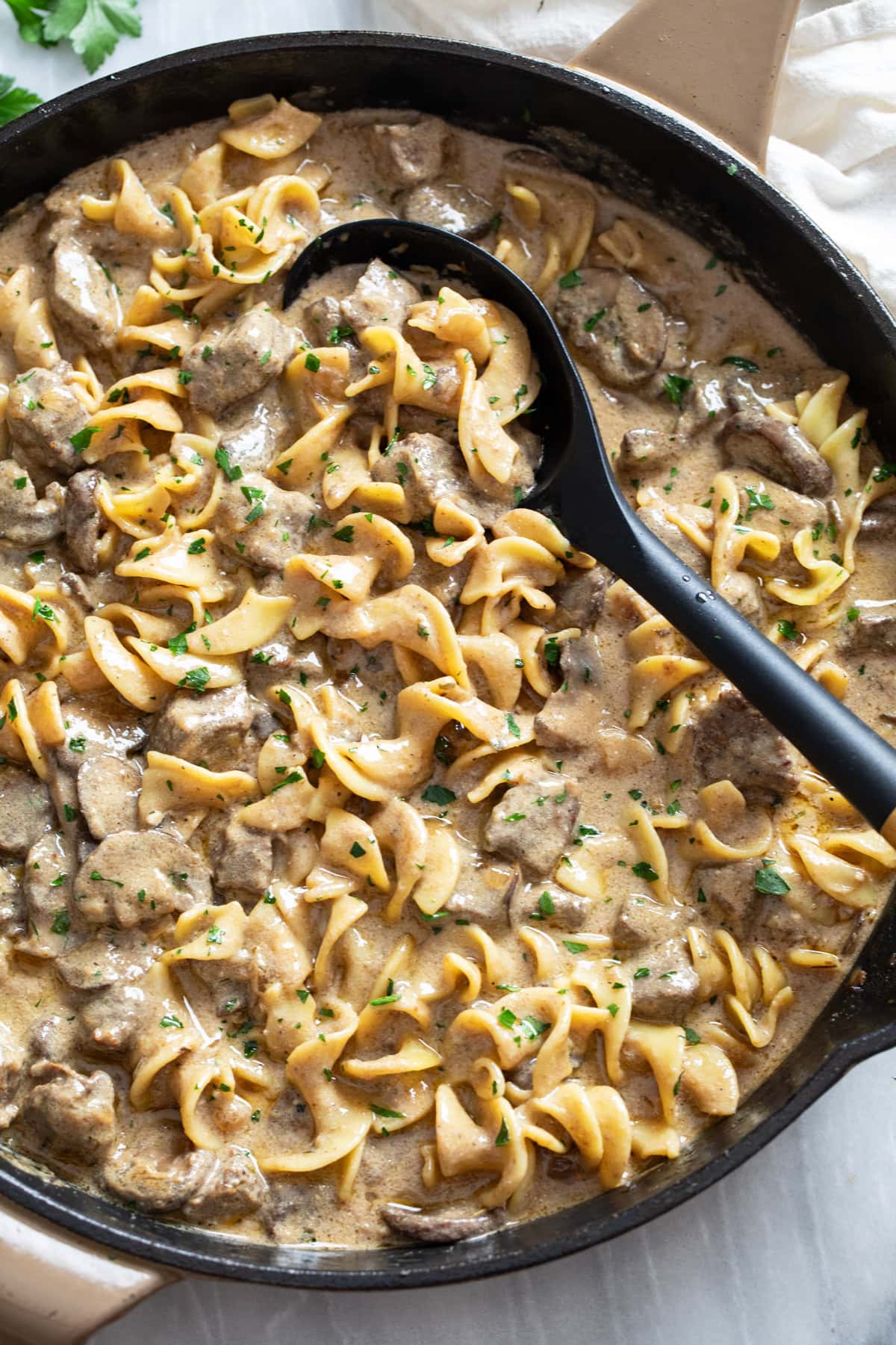Beef Stroganoff in a skillet with a spoon on the side and parsley on top.