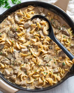 A skillet filled with Beef Stroganoff with Egg Noodles with a serving spoon on the side.
