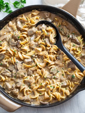 A skillet filled with Beef Stroganoff with Egg Noodles with a serving spoon on the side.