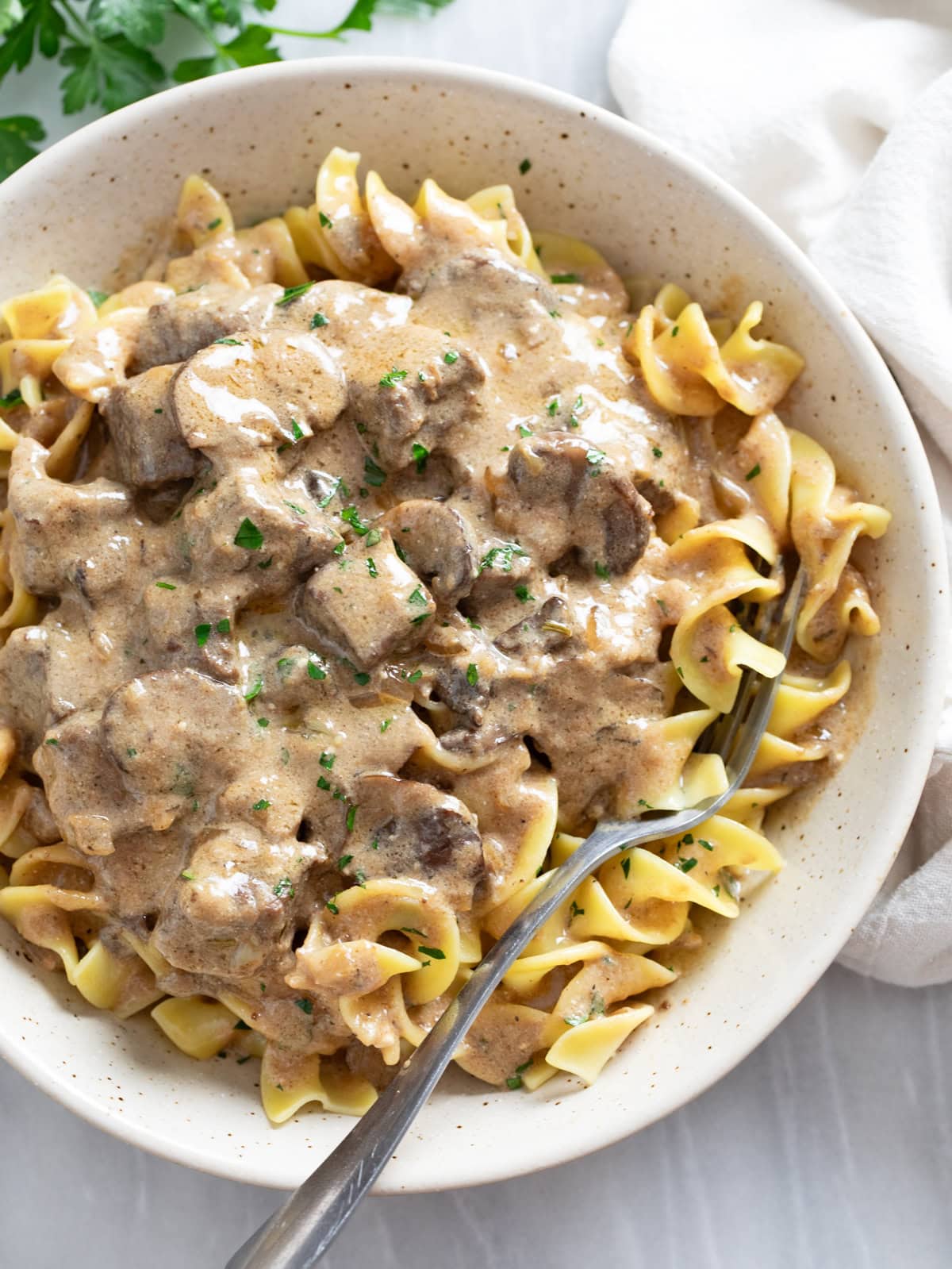 Beef Stroganoff in a white bowl with parsley on top and a fork on the side.
