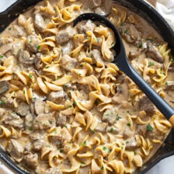 Creamy Beef Stroganoff with egg noodles in a skillet with a black spoon on the side.