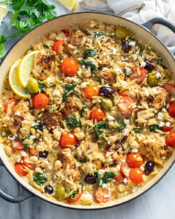 Greek Chicken Orzo in a skillet with sauce, orzo, chicken, chickpeas, spinach, tomatoes, olives, and feta.